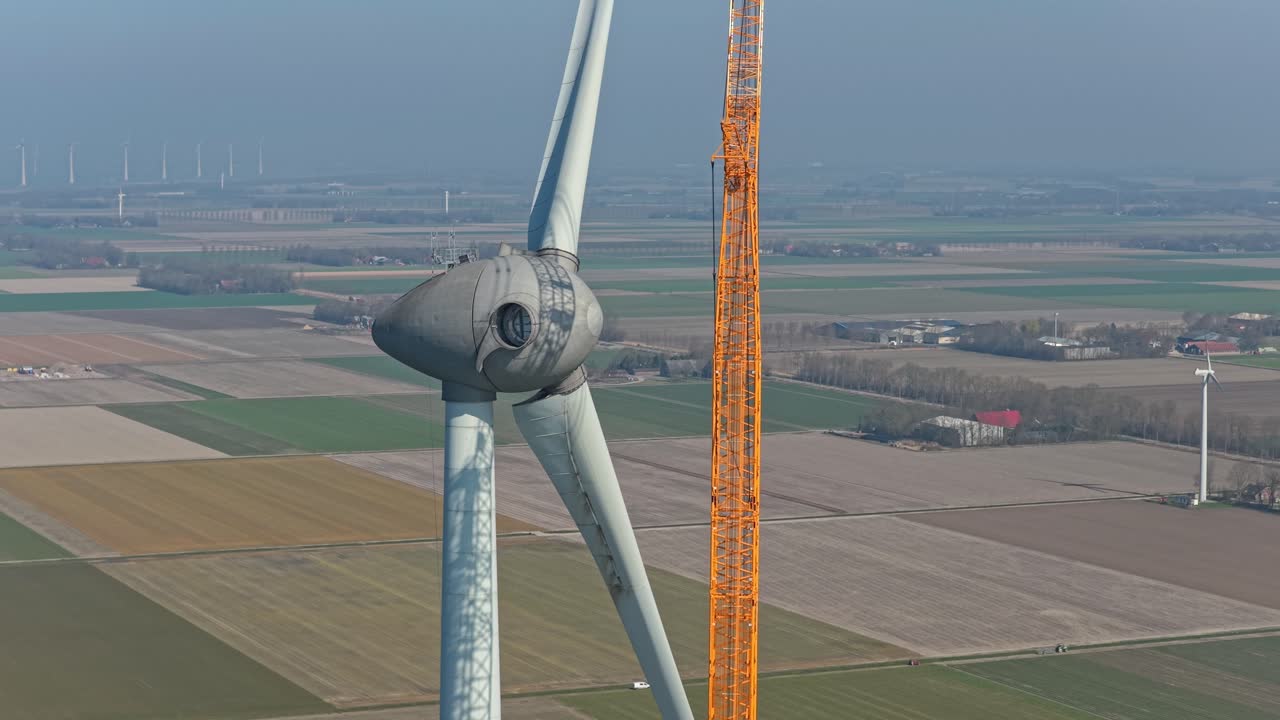 Aerial view of a large crane lifting and installing a massive blade on a wind turbine during construction in the netherlands countryside