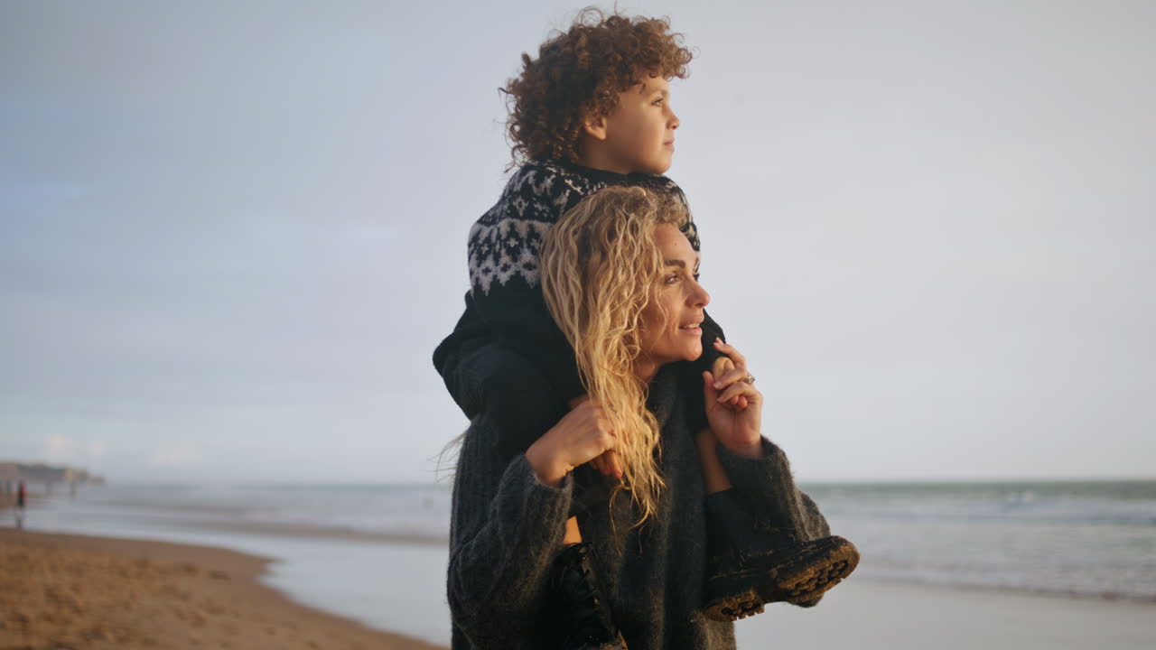 Mother kid going beach together on sunset closeup. Happy boy sit on shoulders