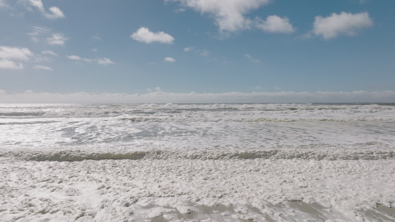 4k toma estacionaria de olas en la playa australiana con espuma marina, espuma oceánica, espuma de playa o espuma creada por la agitación del agua de mar