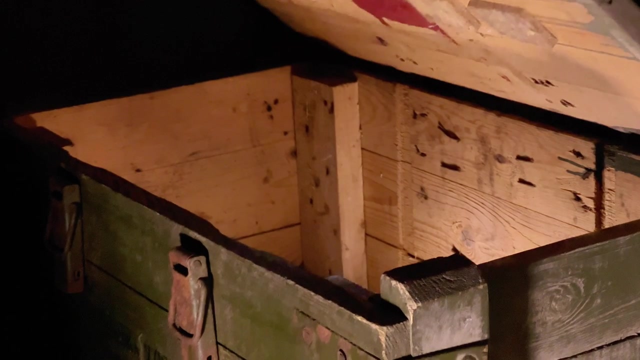 Close-up shot of a hand opening the lid of a vintage wooden ammunition crate in a dark environment illuminated by flashlight. Ideal for cinematic films, games, and documentaries.