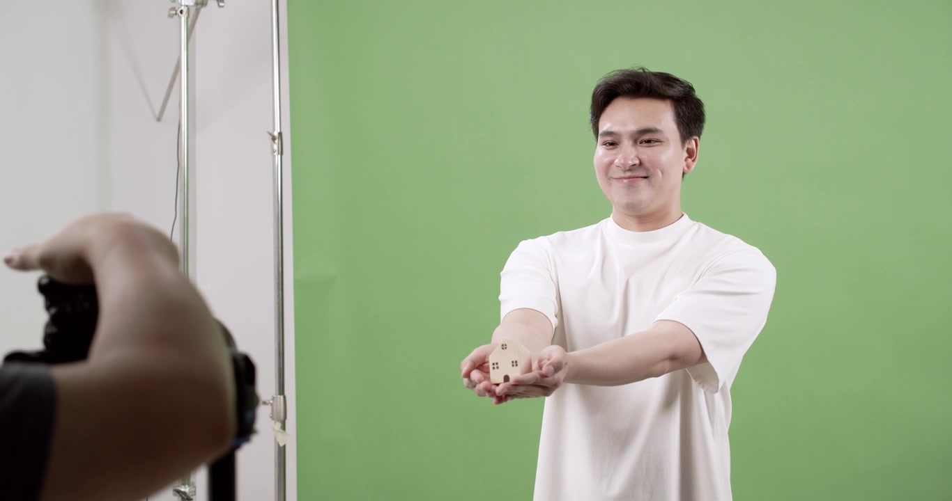 Seorang fotografer mengabadikan seorang model memegang objek kecil di studio dengan latar belakang layar hijau, berfokus pada kreativitas dan ekspresi