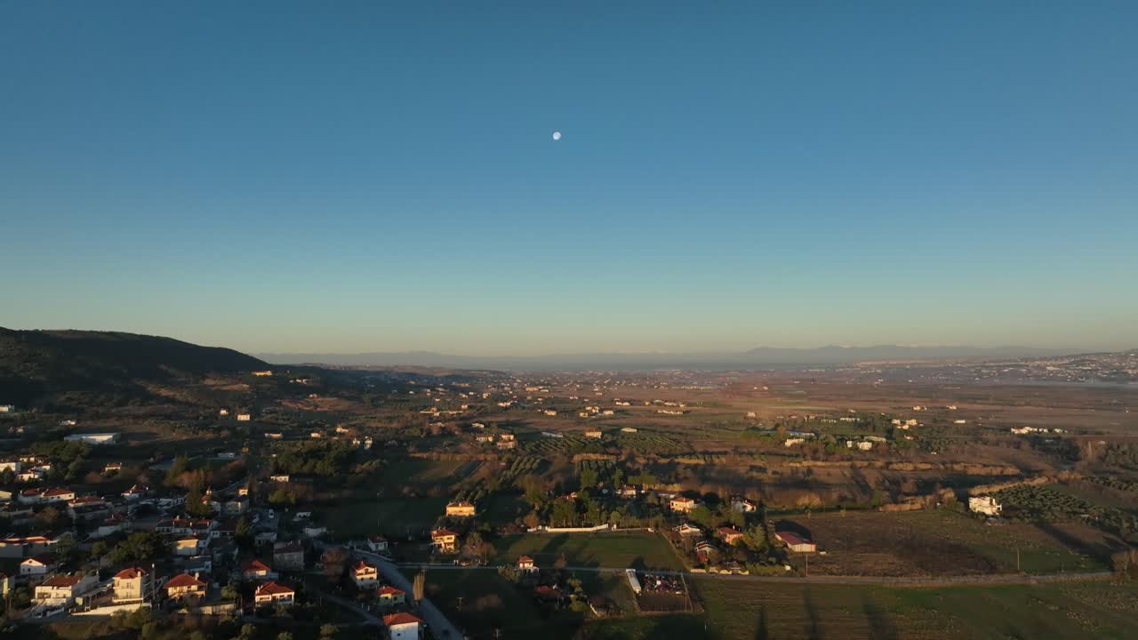 Greek village at sunrise, tilting up to reveal the moon in a vast rural landscape. Greece
