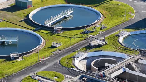 aerial footage pans across a modern wastewater treatment plant, highlighting circular settling tanks, water channels, and industrial infrastructure in bright daylight
