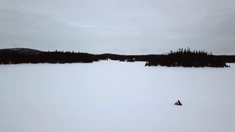 Toma-Aérea-De-Un-Jinete-De-Motos-De-Nieve-Solo-En-La-Inmensidad-De-Un-Lago-Congelado-En-Chibougamau,-Quebec