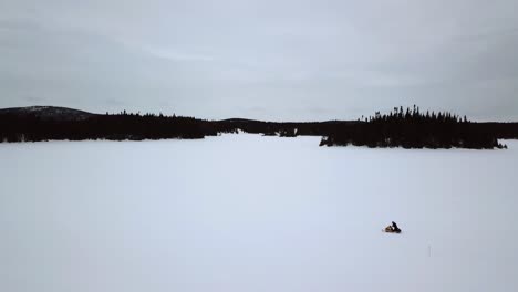 aerial shot of a snowmobile rider alone in the immensity of a frozen lake in chibougamau, quebec