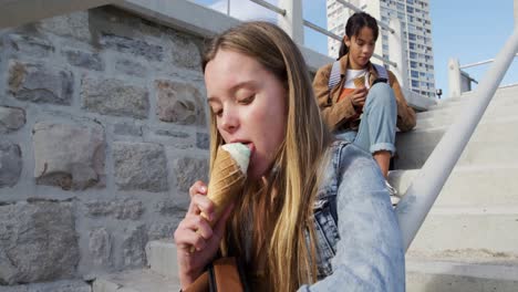 vista lateral de un caucásico y una chica de raza mixta comiendo helado sentada en la escalera