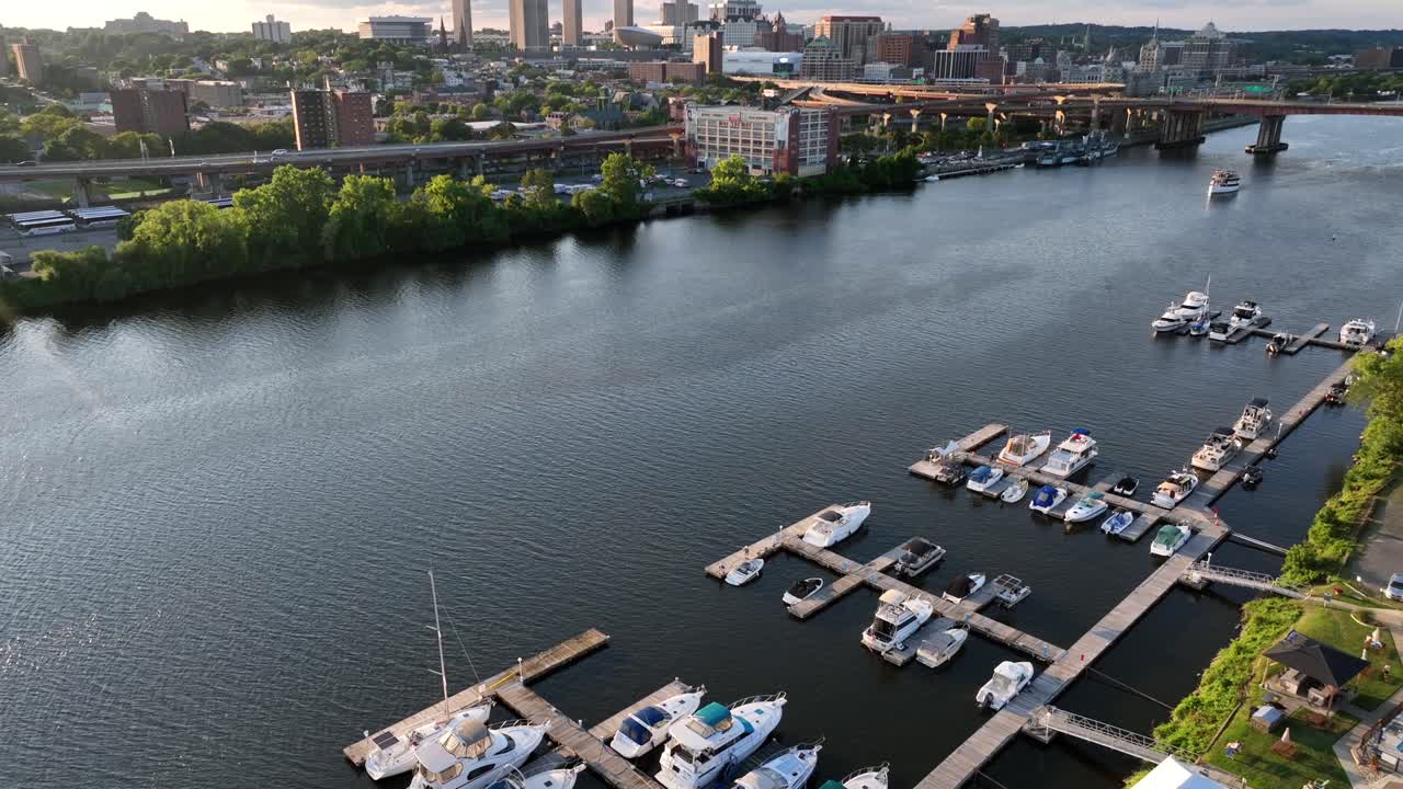 Albany yacht club with swimming pool with river and downtown of albany in background, New York. Aerisl tilt up wide shot. Skyline with skyscraper lighting at golden hour