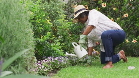 Ältere-Afroamerikanische-Frau-Trägt-Gartenhandschuhe-Und-Gießt-Blumen-Im-Garten