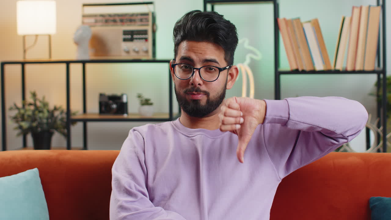 Upset indian man showing thumbs down dislike bad work disapproval dissatisfied feedback at home