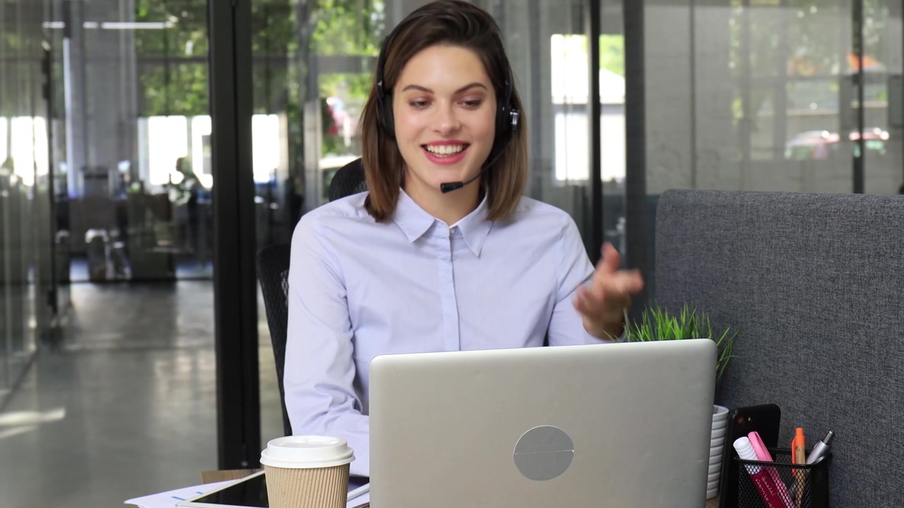 Mujer joven con auriculares hablando en videollamada en una oficina moderna