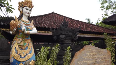 balinese female deity statue in the entrance of sukawati bali temple, purnama beach, religious and worshiping place, indonesia, ancient scripture in axara over stone