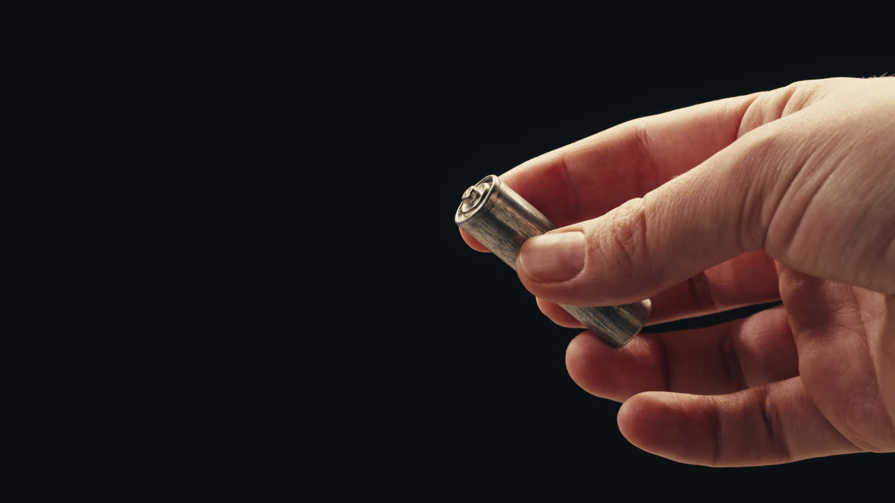 Silver batteries AA and AAA in hands on black background close-up. Double-A battery is a standard size single cell cylindrical dry battery. Batteries are common in portable electronic devices. An AA battery is composed of a single electrochemical cell that may be either a primary battery or a rechar