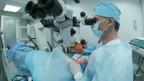 surgeon looking into the microscope at the eye of female patient at the operating room. doctor using microscope during eye surgery process, treatment of cataract and diopter correction.