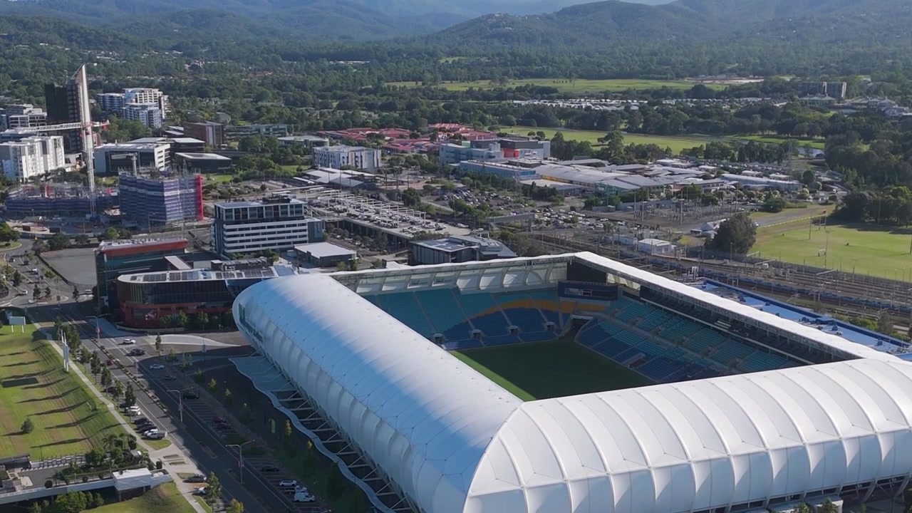 Toma aérea con dron en ángulo alto de un estadio contemporáneo rodeado de desarrollo urbano y vegetación.