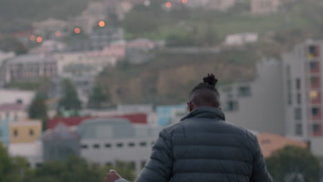 young african american man dancing on rooftop celebrating weekend enjoying cold refreshing beer looking at city skyline
