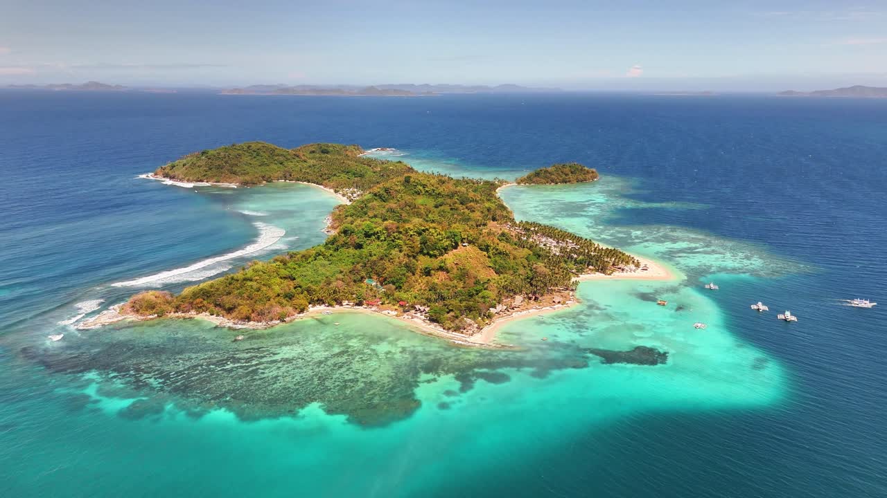 Drone captures Darocotan Island off the coast of Palawan, Philippines, encircled by shallow coral reefs, white sand beaches, and lush tropical vegetation including Cocos nucifera and coastal thickets