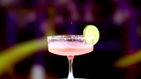 a pink margarita is poured into a glass, garnished with a lime slice, against a colorful background