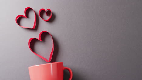 video de taza roja y formas de corazón rojas flotantes, en fondo gris con espacio de copia