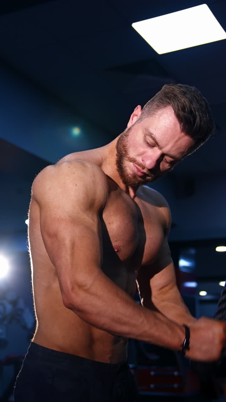 Fitness man pumping up arm muscles. Bodybuilder doing arms exercises with naked torso in gym. Handsome power athletic man at training. Workout indoors. Vertical video