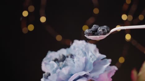 blueberries falling onto white spoon and bouncing off blue flower