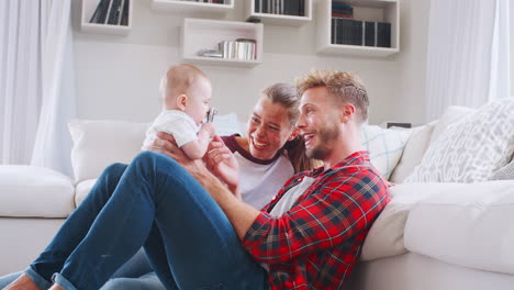 Young-white-couple-sit-playing-with-baby-at-home,-side-view