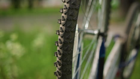 close-up of bicycle placed upside down in a grassy field with its rear tire in focus and slowly rotating, the background, featuring greenery and buildings, is softly blurred