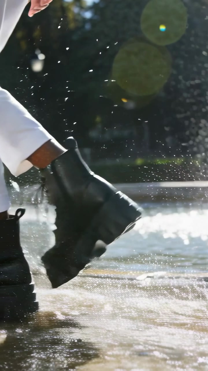 Vertical video: Landing right boot, legs splashing in fountain, white trousers and black boots