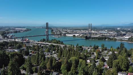 tomada de un avión no tripulado que muestra el puente alex fraser con cielo azul, árboles, casas residenciales y río