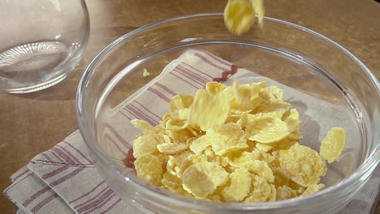 Fiocchi di mais gialli croccanti nella ciotola per una deliziosa colazione mattutina con latte. Slow motion con ripresa rotatoria.