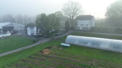 Vista-Aérea-De-La-Asignación-De-Niebla-Con-Invernadero-De-Plástico-Y-Casas-Blancas