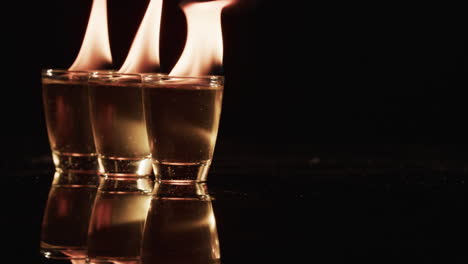 video van verlichte alcohol in glazen met gele vuurvlammen en kopieerruimte op zwarte achtergrond