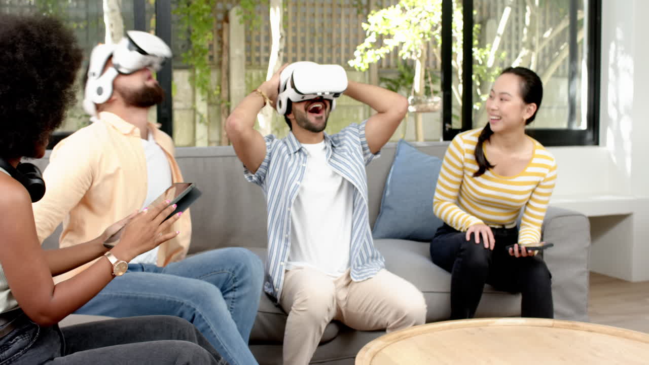 Using VR headset, man sitting on couch with diverse friends laughing and enjoying