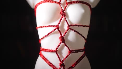 a dark, sensual slow-motion shot of a white mannequin wrapped in red silk shibari ropes, japanese art