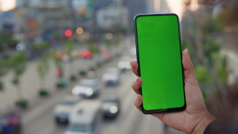 person holding smartphone with green screen displaying outdoors city view
