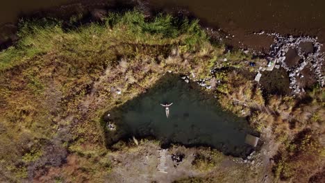 Vista-Aérea-De-Una-Mujer-Flotando-En-El-Agua-En-Un-Bikini-Negro-Disfrutando-De-La-Serenidad-Pura-De-Una-Fuente-Termal-Exterior-En-El-Este-De-Oregon