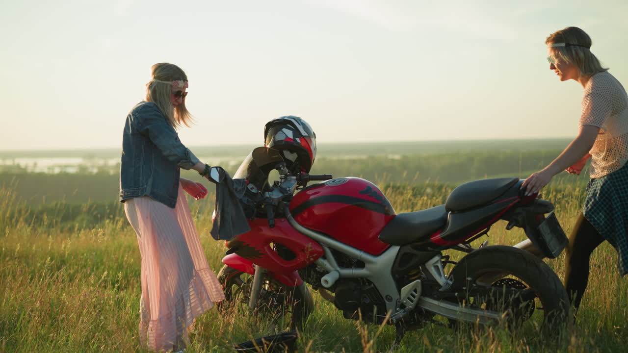 dos mujeres felizmente limpiando una motocicleta roja en un campo abierto de hierba con la toalla en la mano