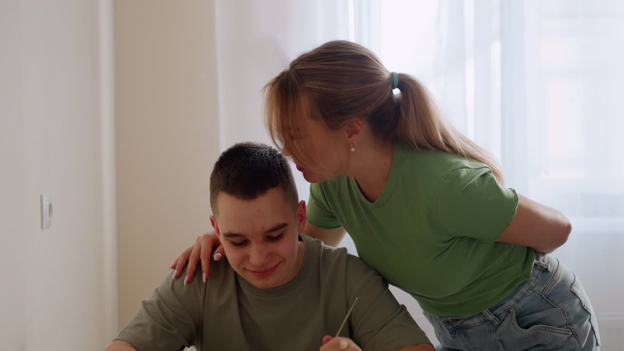 Lad sits at dining table with gentle smile as mum serves him food and shows affection with loving head peck, highlighting family warmth, parental care, and nurturing household mealtime atmosphere