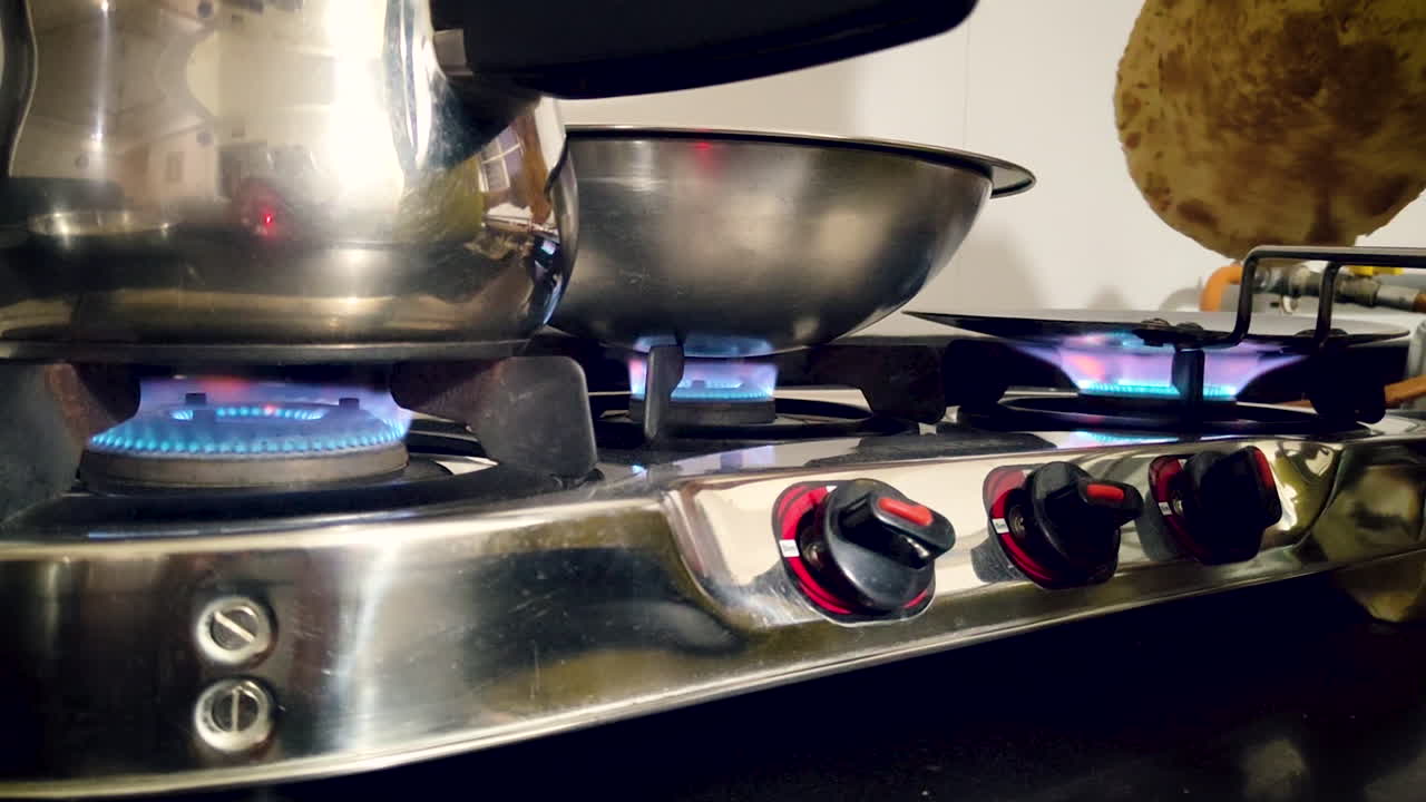 Gaspitten met blauwe vlam, stalen keukengerei en flatbread dat wordt bereid in een thuiskeuken. Bruikbaar voor koken met LPG-gas, huishouden, energie en content over het huiselijk leven.