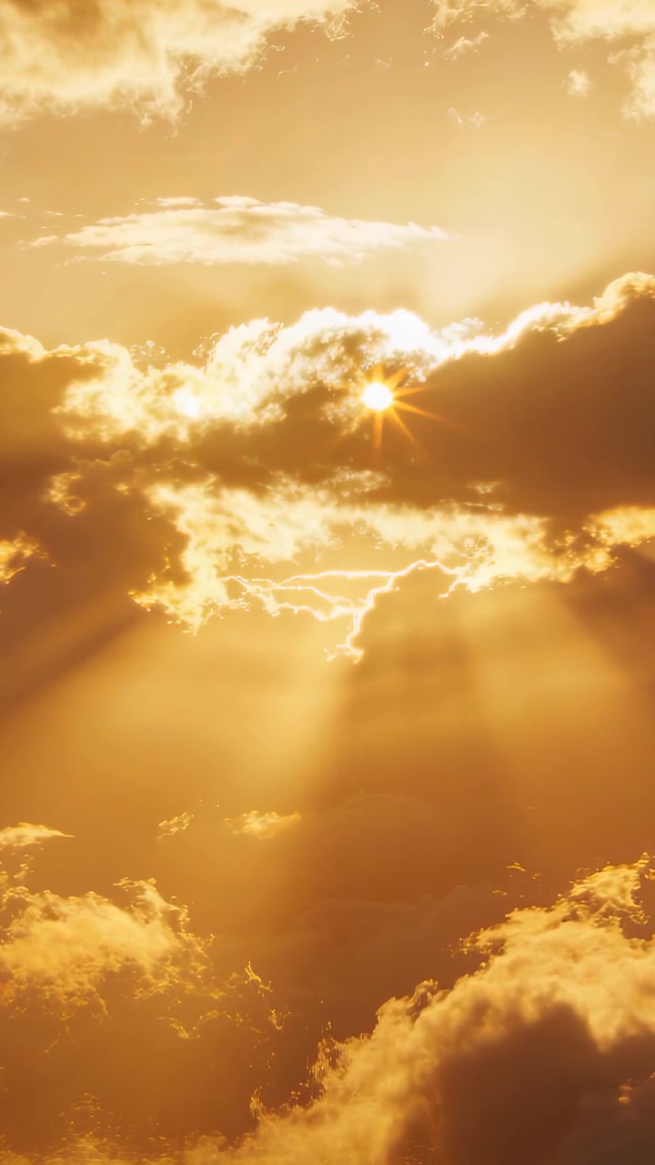 Vertikales Video: Aufhellung hinter oberer Wolke enthüllt Sonnenscheibe und Sonnenstrahlen über goldenem Himmel.