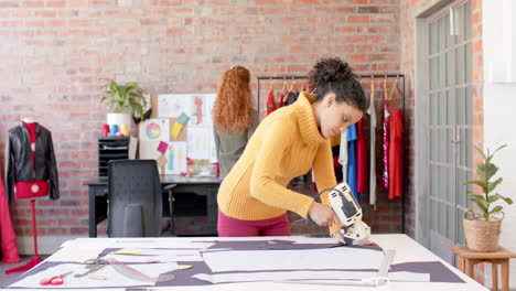 biracial female fashion designer using rotary fabric cutter in studio, slow motion