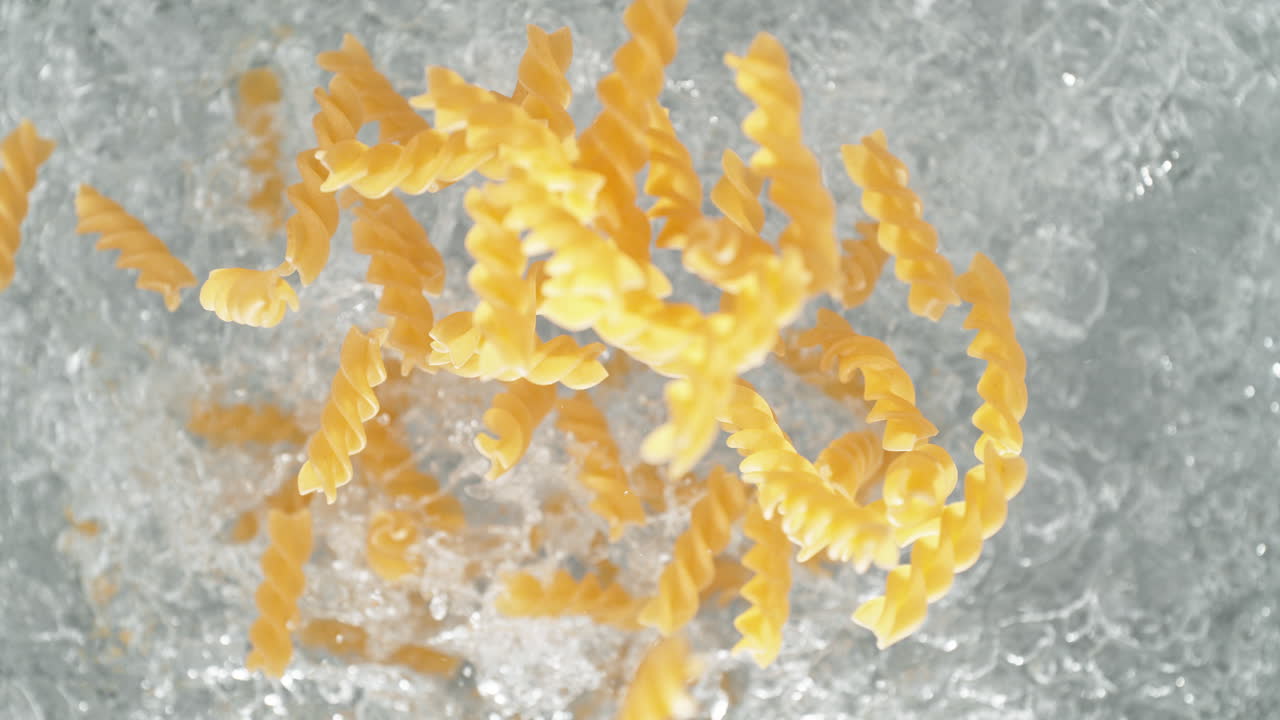 Fusilli Pasta Falling Into Pot Of Boiling Water Making A Splash In Slow Motion, Table Top View