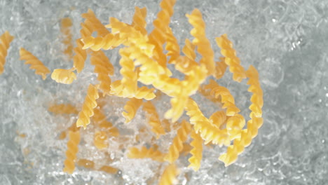 la pasta de fusilli cayendo en una olla de agua hirviendo haciendo un salto en cámara lenta, vista de la mesa