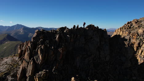 vista aérea de un excursionista solitario de pie en una colina rocosa con una increíble vista del paisaje montañoso soleado, disparo de drone en órbita