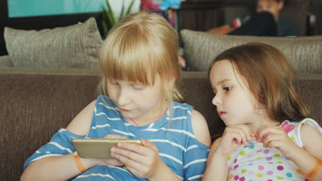 little sisters rest on the sofas at a tourist hotel on the retsepshina play games on the mobile phon