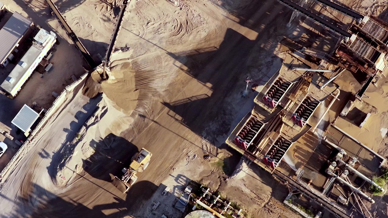 A gravel and sand pit in operation, screw washers and wheel loader at sunrise with long shadows - straight down aerial perspective
