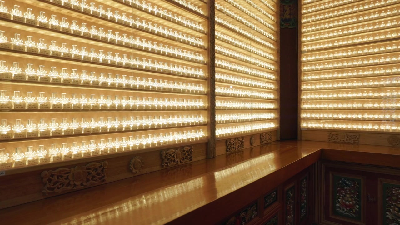 File di piccole candele votive luminose all'interno della sala del santuario del Tempio Haedong Yonggungsa a Gijang, Busan, Corea del Sud. Ripresa con zoom
