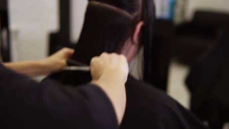Unrecognizable-hair-stylist-who-practices-in-a-beauty-salon-combs-wet-hair-in-order-to-make-a-stylish-haircut-and-change-the-image-of-the-client---woman-with-brown-hair.-Rare-view-of-a-brunette-female-client-with-long-wet-hair