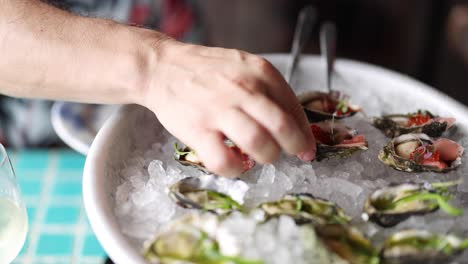 hands garnishing fresh oysters with toppings