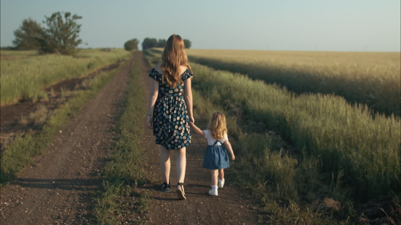 madre y hija felices caminando juntas afuera en el campo, en un camino de tierra en una granja en el atardecer de verano teniendo una familia positiva y amorosa o un momento del día de la madre en cámara lenta cinematográfica