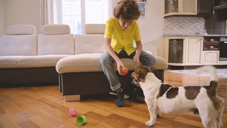 blond boy with curly hair sitting on the couch while playing with his dog